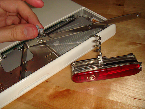 Removing the metal shield that runs across the top-edge of the battery compartment of the 2006 Polycarbonate MacBook.